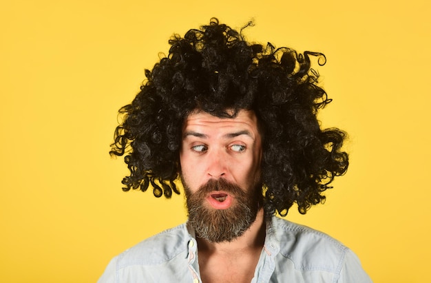 Surprised man in curly wig. Surprised bearded man. Portrait of surprised man. Isolated. Wig. Colorfull hair. Emotions.