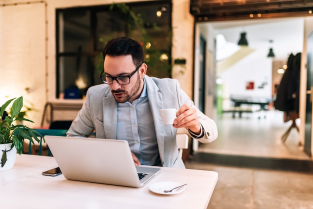 Surprised man looking at laptop while holding a coffee cup in the cafe.