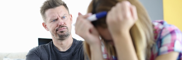 L'uomo sorpreso guarda la donna con la testa china e tenendo il test di gravidanza. gravidanza non pianificata nel concetto di relazione