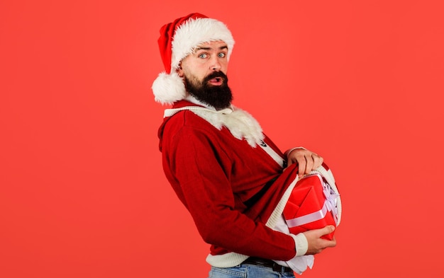 Удивленный мужчина в костюме санта-клауса прячет подарочную коробку под свитером, рождественский подарок в канун нового года