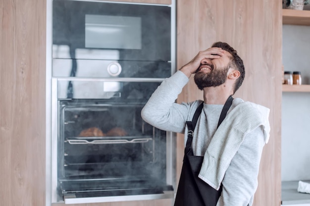 Surprised man standing near the oven with burnt croissants