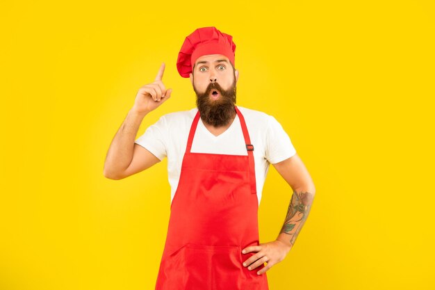 Surprised man in toque and apron got idea keeping finger raised yellow background chef