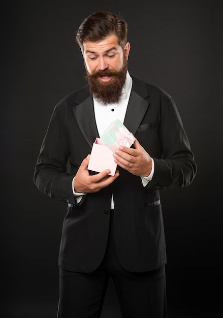 Surprised man in tuxedo bow tie formalwear on black background with box birthday