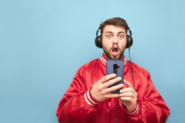 Surprised man with a beard in the headphones, holds a smartphone in his hands