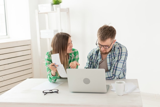 Surprised married couple. Husband and wife are considering bills for paying an apartment and are shocked at the amount received by writing down the results in their home accounting in a laptop.