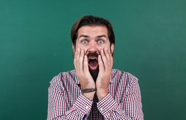 Surprised mature bearded man teacher in school classroom with blackboard back to school