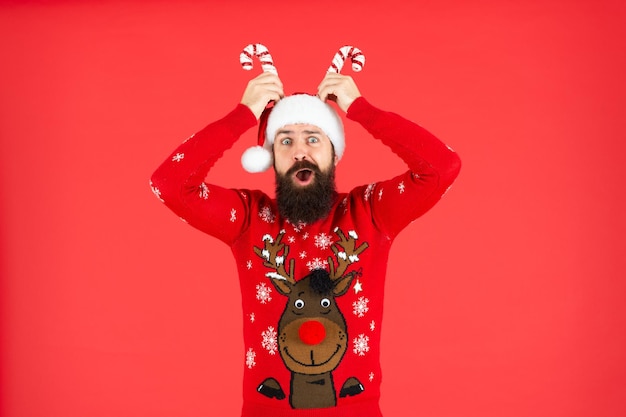 Surprised mature guy in santa hat and sweater on red background new year