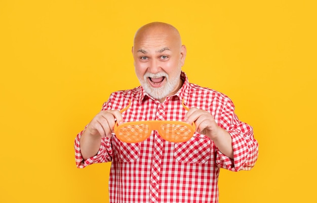 Surprised mature man with party glasses on yellow background