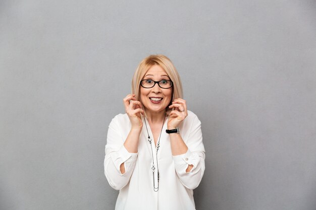 Surprised middle-aged blonde woman in shirt and eyeglasses rejoices