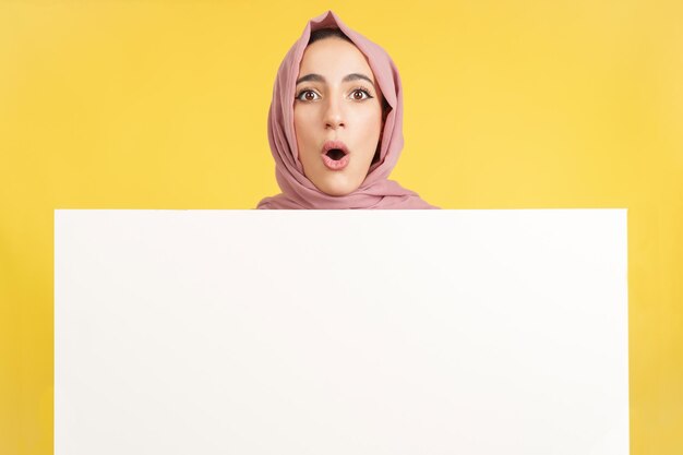 Surprised muslim woman holding a blank panel