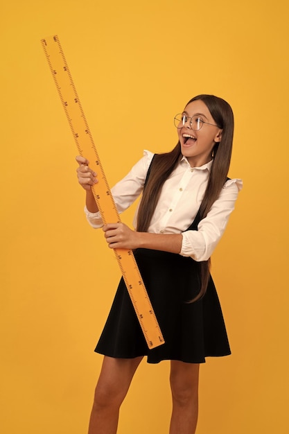 Surprised nerd teen girl in uniform and glasses hold mathematics ruler for measuring back to school