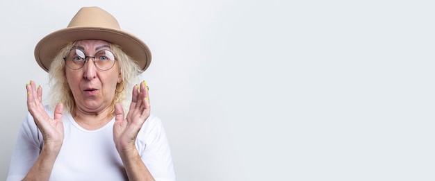 Surprised old woman in a hat on a light background. Banner.