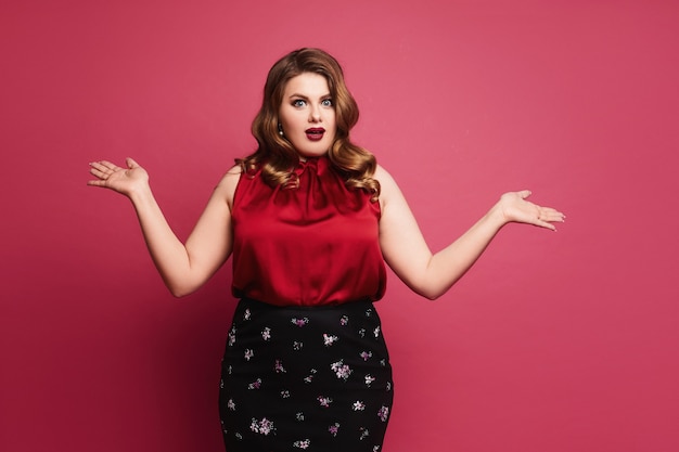 Surprised plus size model with bright makeup in red satin blouse and black skirt