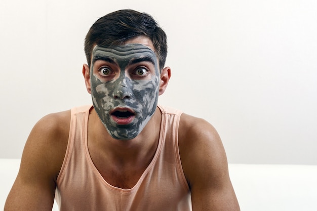 Surprised portrait of a man in a clay mask on his face. skin care. copyspace