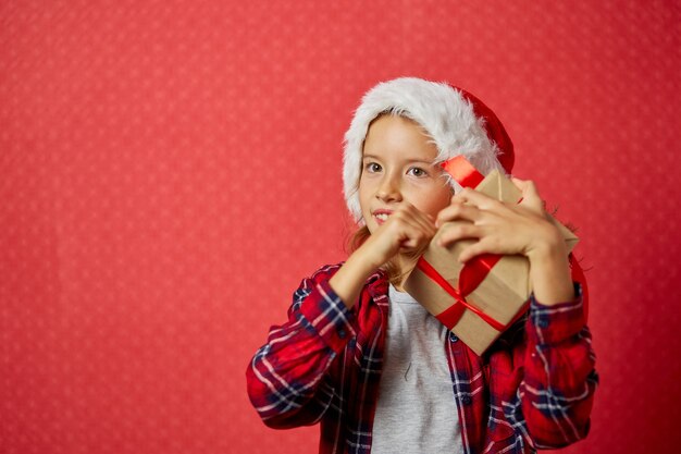 クリスマスプレゼントを保持しているサンタの帽子をかぶった驚きとポジティブな少女