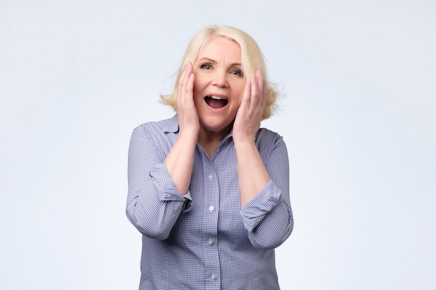 Surprised senior blonde woman with hands up being amazed