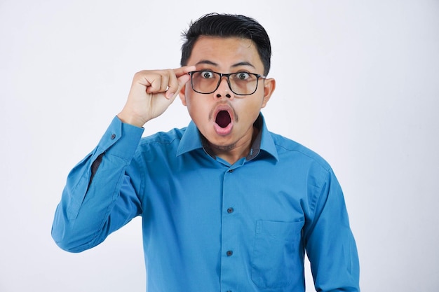 青いシャツを着て眼鏡をかけた驚いたまたはショックを受けたアジア人男性口を開け手を握る