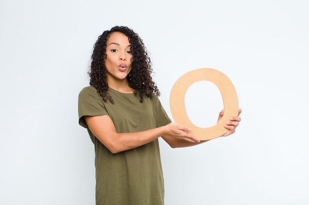 Photo surprised, shocked, amazed, holding the letter o of the alphabet to form a word or a sentence.