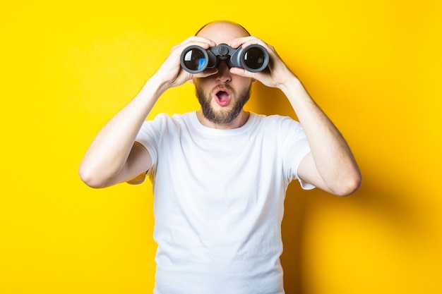 Surprised shocked bearded young man looks through binoculars