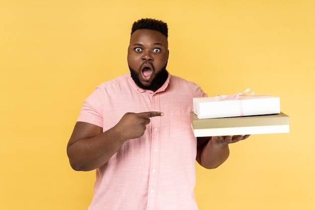 Surprised shocked man holding and pointing at gift boxes looking at camera with open mouth