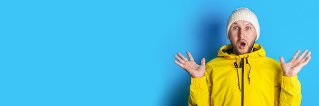 Surprised shocked young man in a yellow jacket on a blue background. Banner.