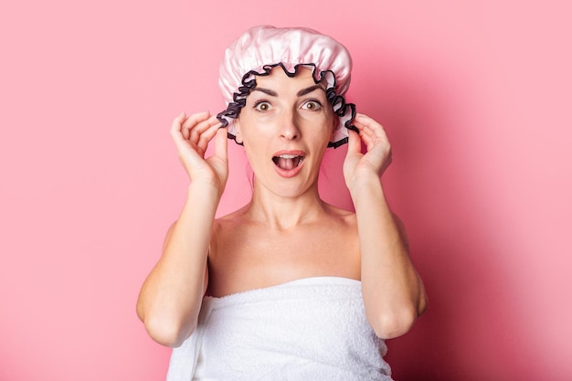 Surprised shocked young woman in pink shower cap on pink background