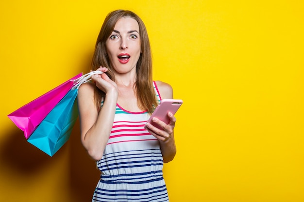 Surprised shocked young woman with phone holding shopping bags 