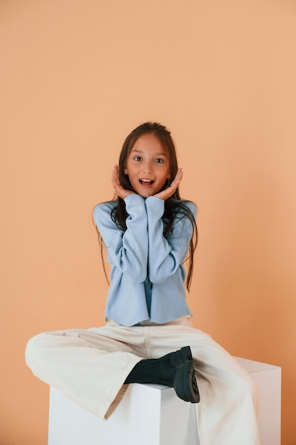 Surprised sitting on white cube cute young girl is in the studio against background