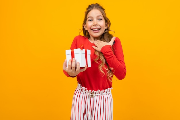 Surprised smiling beautiful girl with a gift box on yellow with copy space