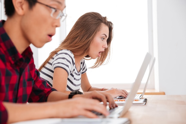 Photo surprised students looking at laptops in a classroom