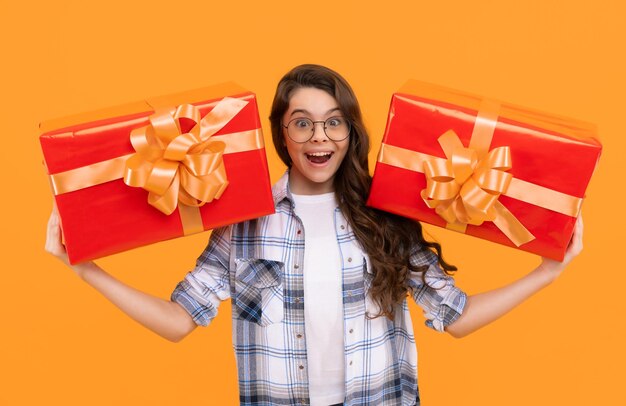 Surprised teen child with present isolated on yellow background teen child in glasses with present studio shot of teen child hold present teen child holding box of present