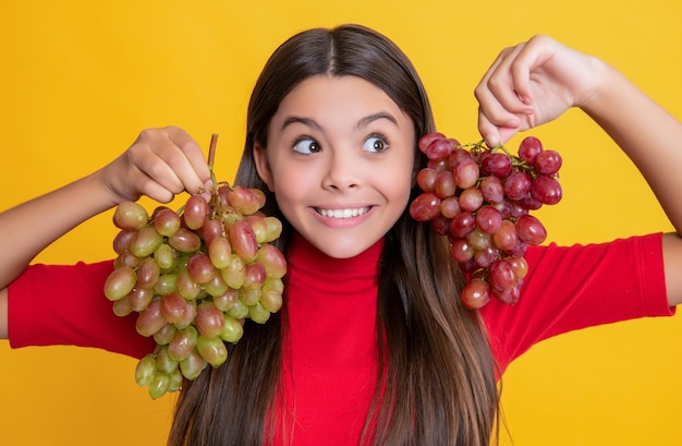 Surprised teen girl hold bunch of grapes on yellow background