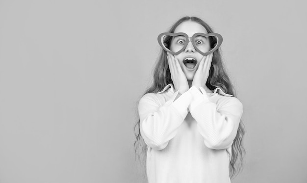 Surprised teen girl in party glasses on blue background with copy space fancy