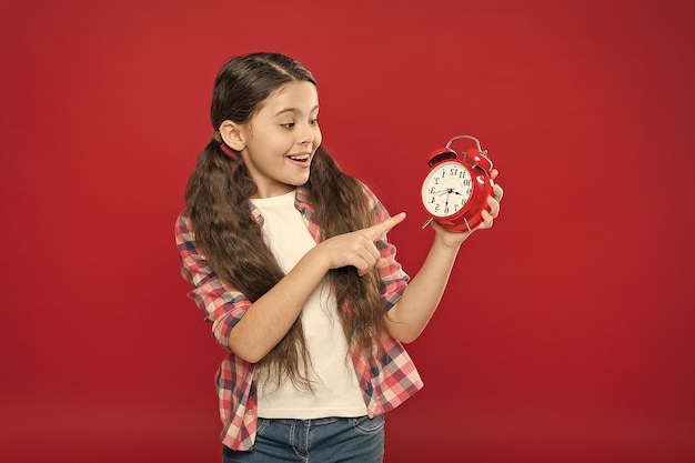 Удивленная девочка-подросток показывает время на распродажах ретро-будильника
