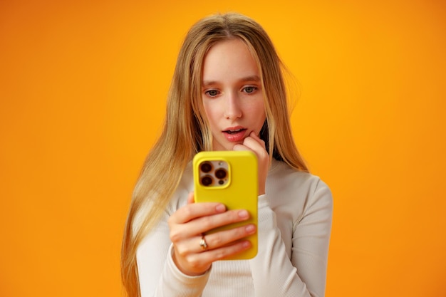 Foto ragazza teenager sorpresa che usa il telefono cellulare su sfondo giallo da vicino