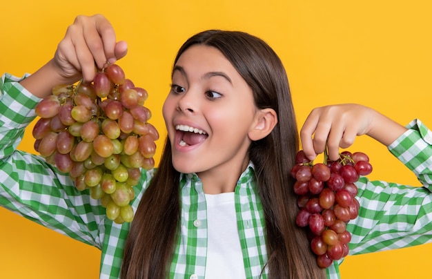 Foto ragazza teenager sorpresa con grappolo d'uva su sfondo giallo