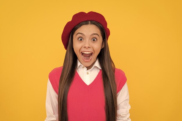 Surprised teen school girl in french beret on yellow background happiness