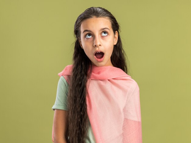 Surprised teenage girl wearing shawl looking up with open mouth isolated on olive green wall with copy space