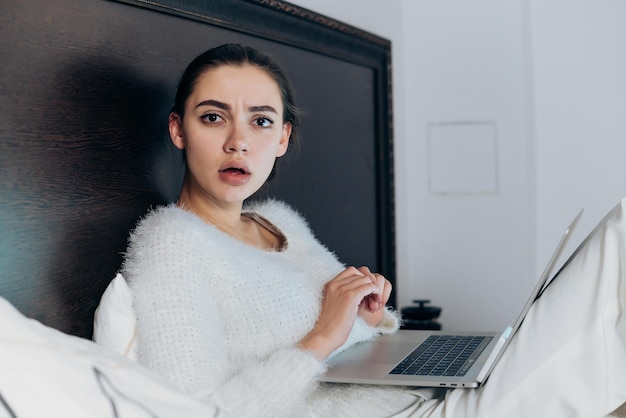 Surprised tired girl freelancer sitting in bed at night working on laptop