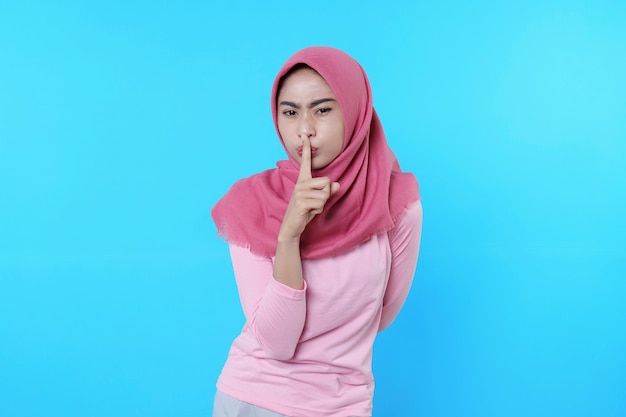 Surprised wearing hijab woman keep secret and ask for silence, presses index finger to lips