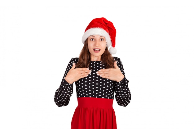 Surprised woman in dress holding hands on breast smiling being touched and pleased. emotional girl in santa claus christmas hat isolated