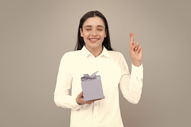 Surprised woman holding gift funny girl crossed fingers for good luck smiling beautiful young