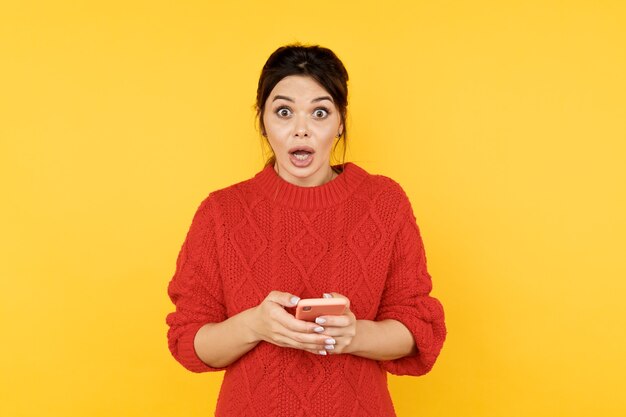 Surprised woman holding phone with opened mouth isolated.