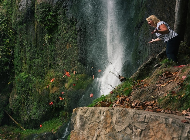 surprised woman looking at autumn leaves falling by waterfall
