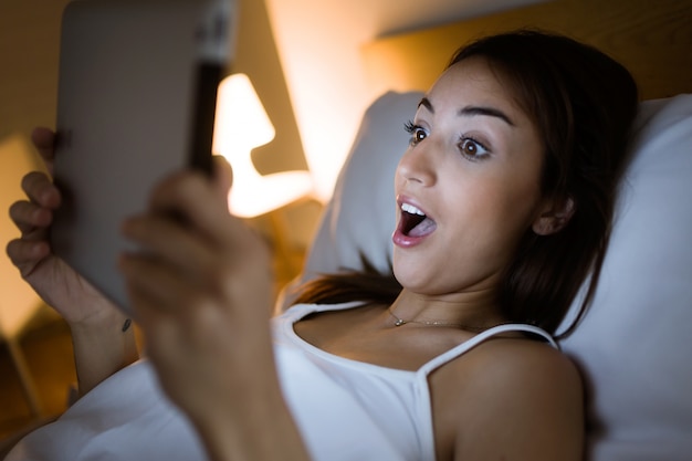 Surprised woman looking her digital tablet in the bed at night.