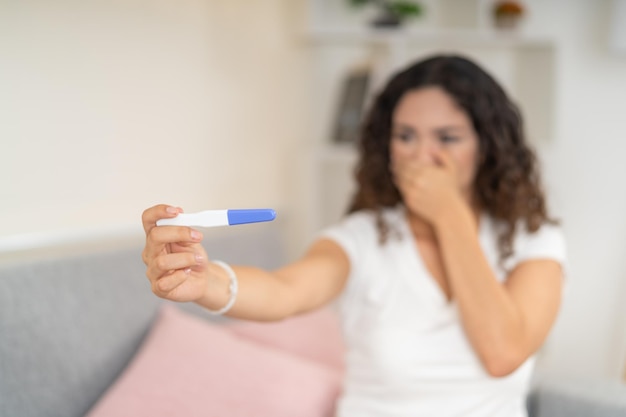 Photo surprised woman looking at a pregnancy test sitting at home