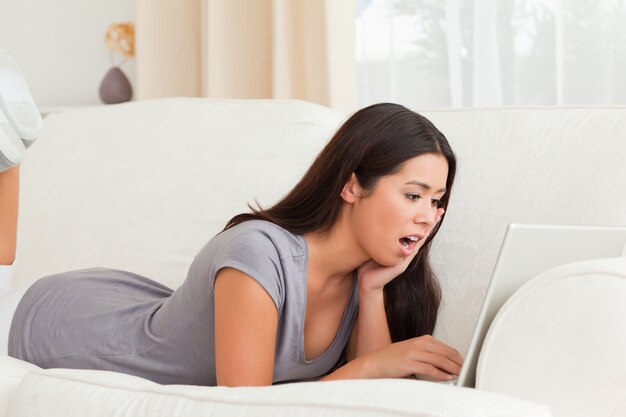 Surprised woman lying on sofa with notebook in front of her