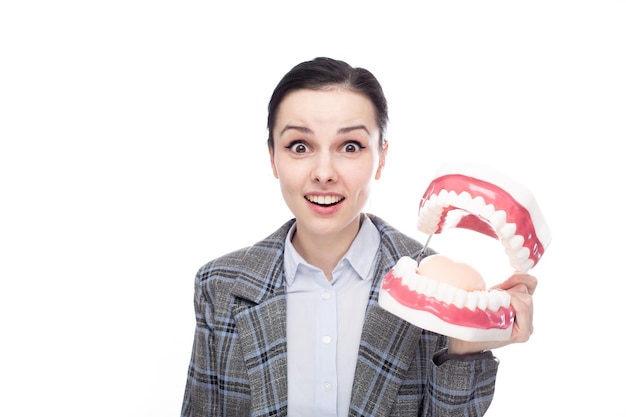 surprised woman in an office suit holds a dental model of the jaw in her hands white background