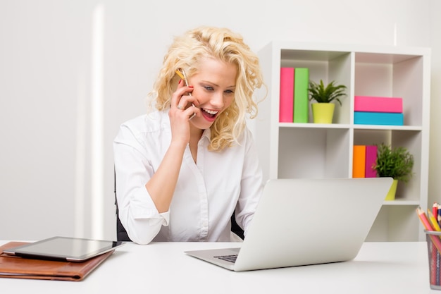 Surprised woman at the office talking on the phone and working on computer