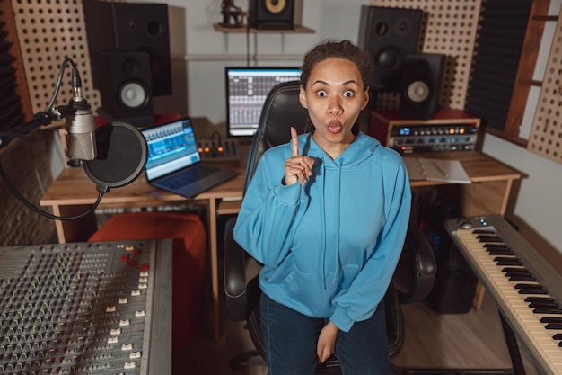 Surprised woman points finger up while sitting in a sound engineer room in modern broadcasting